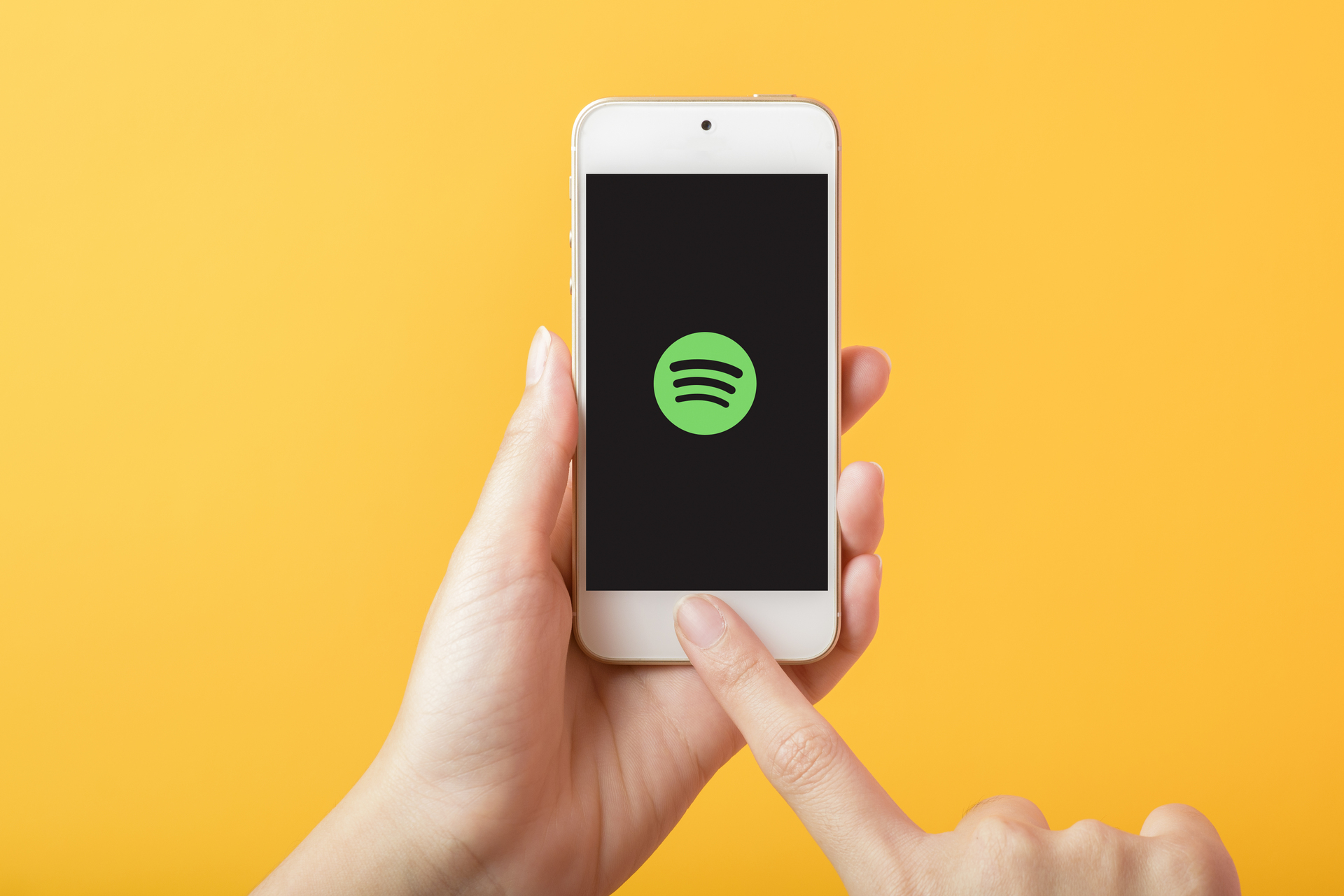 Ein Smartphone, gehalten in einer Hand gegen einen orangefarbenen Hintergrund, mit dem Spotify-Logo auf dem Bildschirm beim Start der App